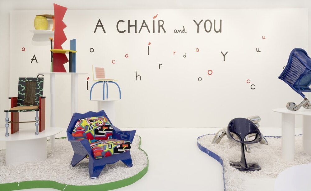 Several colourful chairs on paper islands, written on the wall A CHAIR AND YOU